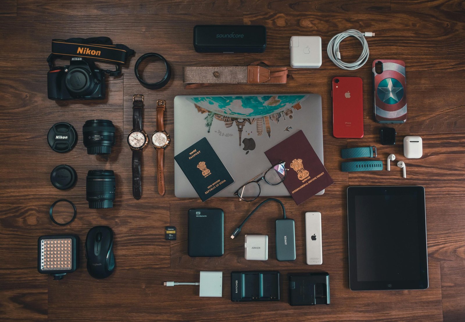 Flat lay of travel essentials including gadgets, passports, and camera on wooden surface.